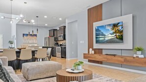 A modern living room with a large TV, a dining area, and a kitchen in the background. - FL- 1844 GOBI DR (Kissimmee)