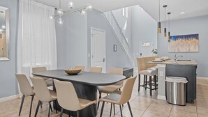 A modern kitchen with a central island, a dining area with a round table, and a staircase leading to an upper level. - FL- 1844 GOBI DR (Kissimmee)