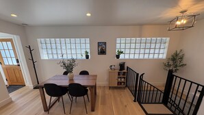 A dining area with a wooden table and chairs, a coffee maker, and a cabinet with mugs and cups. There are windows with blinds and a staircase with a black railing. - Queen Anne City Escape - 1 bed, 1.5 bath, dog friendly, 1 parking space (Seattle)