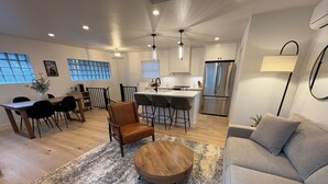 A modern kitchen with a central island, a dining area with a wooden table and chairs, and a living area with a sofa and a coffee table. - Queen Anne City Escape - 1 bed, 1.5 bath, dog friendly, 1 parking space (Seattle)