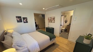 A modern bedroom with a large bed, bedside tables, a desk, and a bathroom visible through an open door. - Queen Anne City Escape - 1 bed, 1.5 bath, dog friendly, 1 parking space (Seattle)