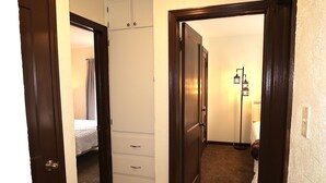 Een hal met een bed, een witte dressoir en een vloerlamp.