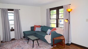 Een woonkamer met een hoekbank, een bijzettafeltje, een vloerlamp en een kamerkleed met een patroon.