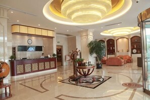 Een hotel lobby met een receptiebalie, een zithoek en een grote kroonluchter.