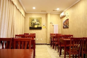 A dining area with wooden tables and chairs, a painting on the wall, and an air conditioning unit. - GreenTree Inn (Shanghai Jiangyue Road Metro Station) (Shanghai)