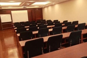 A conference room with rows of tables and chairs, a whiteboard, and a projection screen.