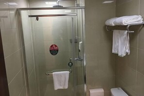 Een douchecabine met glazen wanden, een handdoekrek en een bord, een toilet en een handdoekrek met opgevouwen handdoeken.