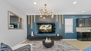 A modern living room with a flat-screen TV, dark cabinetry, and a stylish chandelier. - FL- 1904 Nice Ct (Kissimmee)