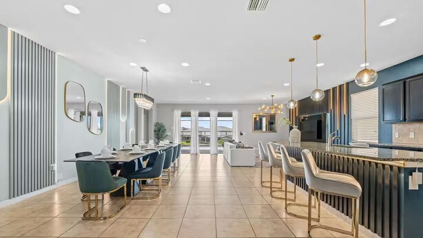 A modern kitchen with a central island, bar seating, and a dining area with a long table and chairs.