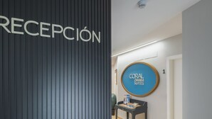 A reception area with a vertical panel labeled "RECEPCIÓN" and a circular sign for "CORAL ZAHARA SUITES".