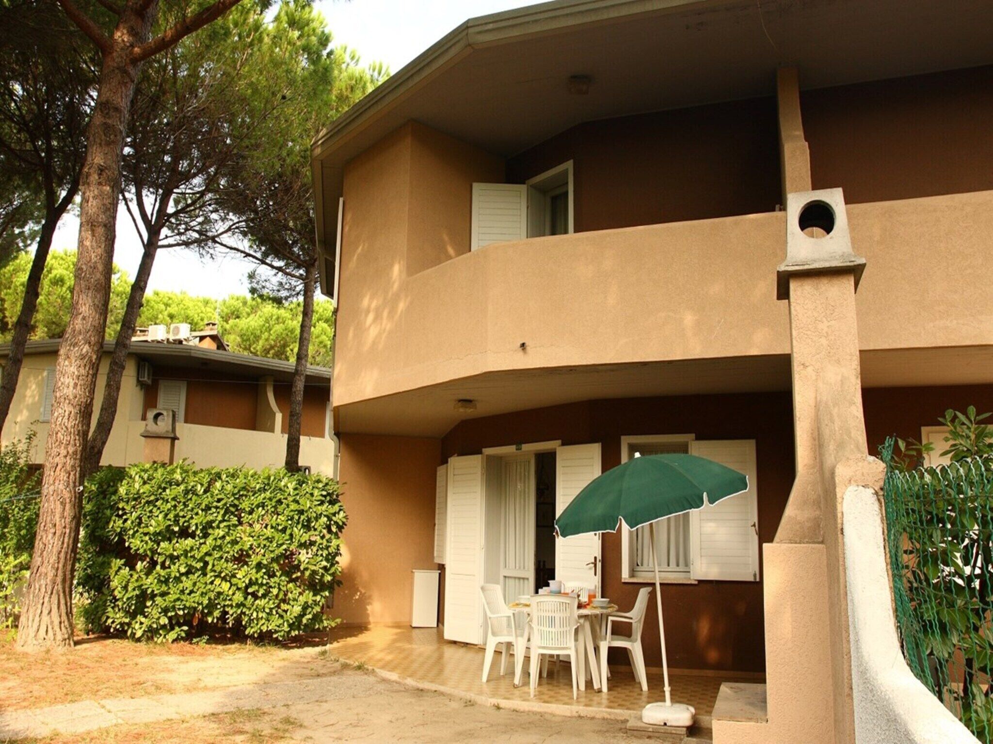 A two-story building with a balcony, outdoor seating area, and a green umbrella.