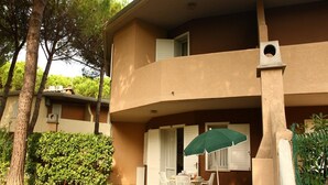 A two-story building with a balcony, outdoor seating area, and a green umbrella. - Cozy Stay With Shared Pool (San Michele al Tagliamento)