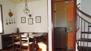 A dining area with a wooden table and chairs, a hanging light fixture, and a kitchen with a refrigerator and cabinets. - Cozy Stay With Shared Pool (San Michele al Tagliamento)