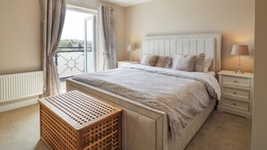 Une chambre à coucher avec un grand lit, deux tables de chevet avec des lampes, un banc en bois et une vue par une fenêtre avec des rideaux.