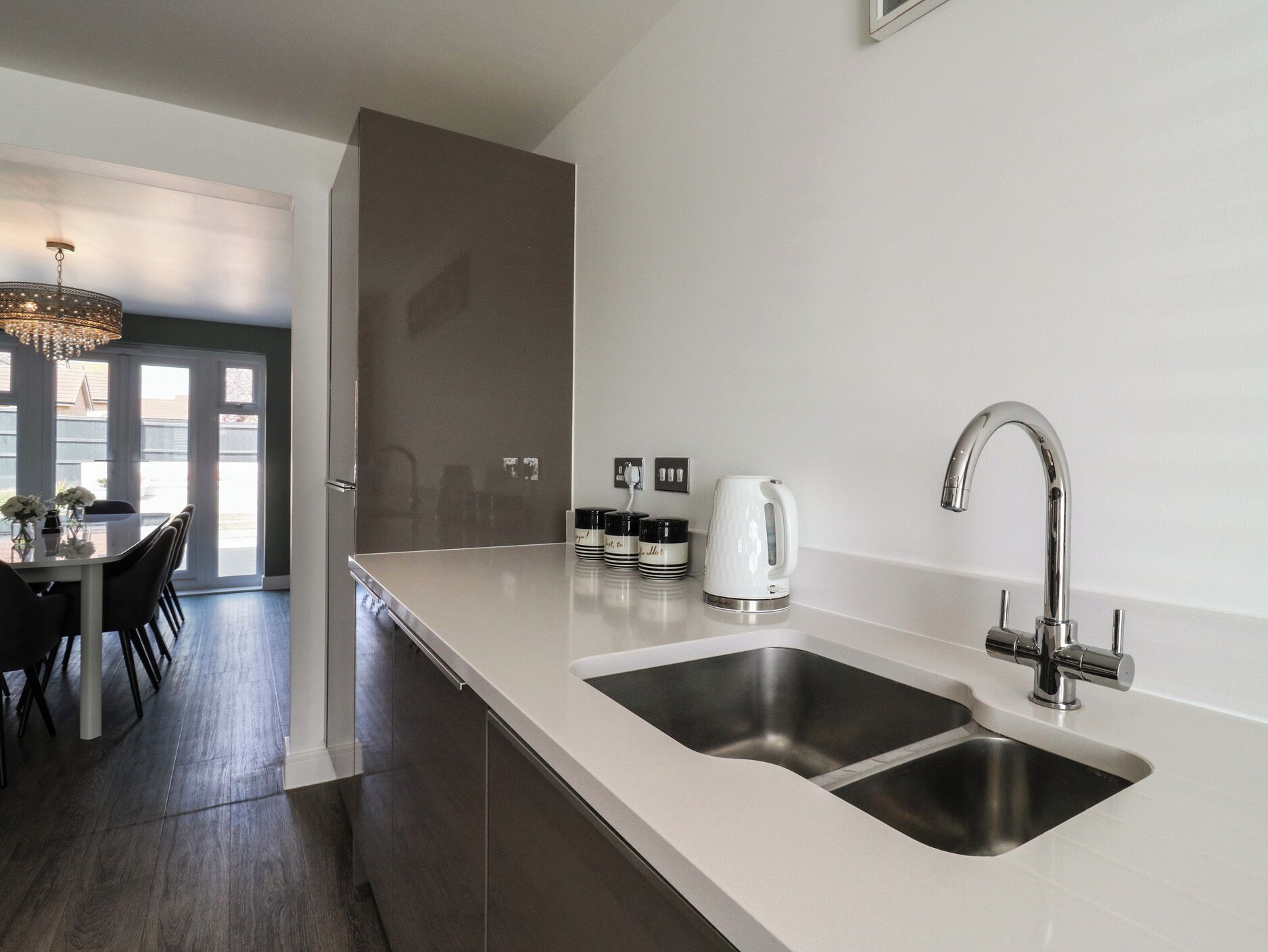 A modern kitchen with a double sink, stainless steel appliances, and a dining area with a chandelier.