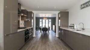 Une cuisine moderne dotée d’appareils électroménagers en acier inoxydable, un coin repas agrémenté d’un lustre, et une vue sur le salon.