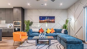 A modern living room with a sectional sofa, a coffee table, and a cityscape painting on the wall. - [Royal Luxury] Dallas Oak Lawn Lux - 8 bedrooms 7 baths ,2 Gamerooms, 2 Hot Tubs (Dallas)