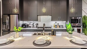 A modern kitchen with dark cabinets, stainless steel appliances, and pendant lighting. - [Royal Luxury] Dallas Oak Lawn Lux - 8 bedrooms 7 baths ,2 Gamerooms, 2 Hot Tubs (Dallas)