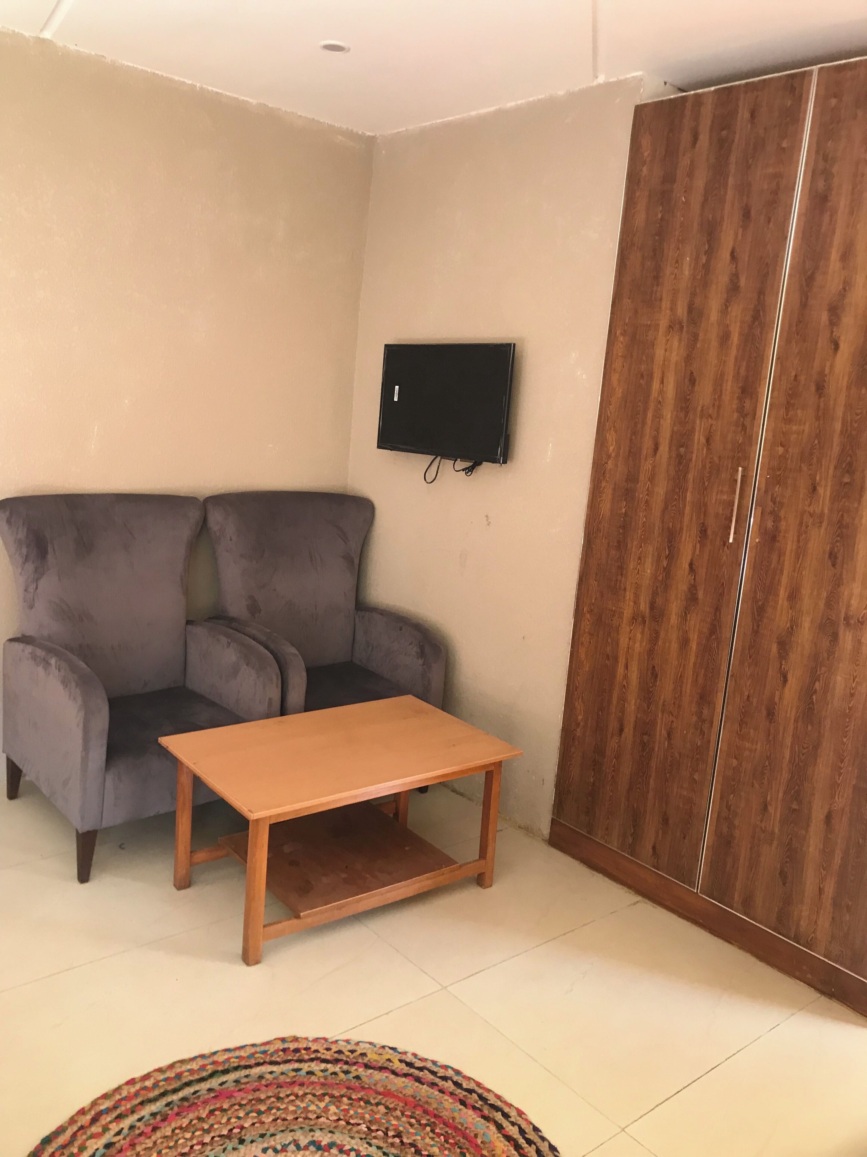 A living room with a grey sofa, a wooden coffee table, a TV mounted on the wall, and a wooden wardrobe.