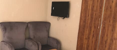 A living room with a grey sofa, a wooden coffee table, a TV mounted on the wall, and a wooden wardrobe.