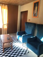 A living room with a checkered floor, a wooden coffee table, two blue sofas, and a painting on the wall.