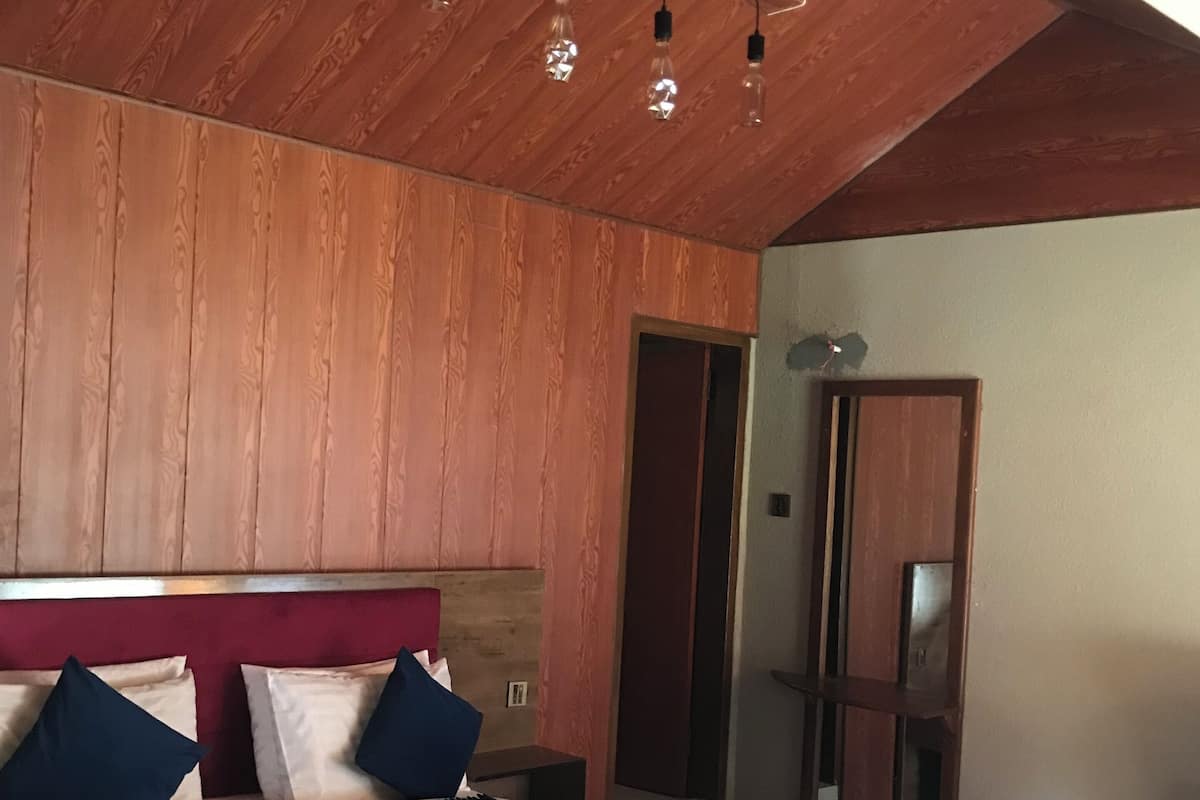 A bedroom with a wooden ceiling, a bed with white and blue bedding, and a nightstand.