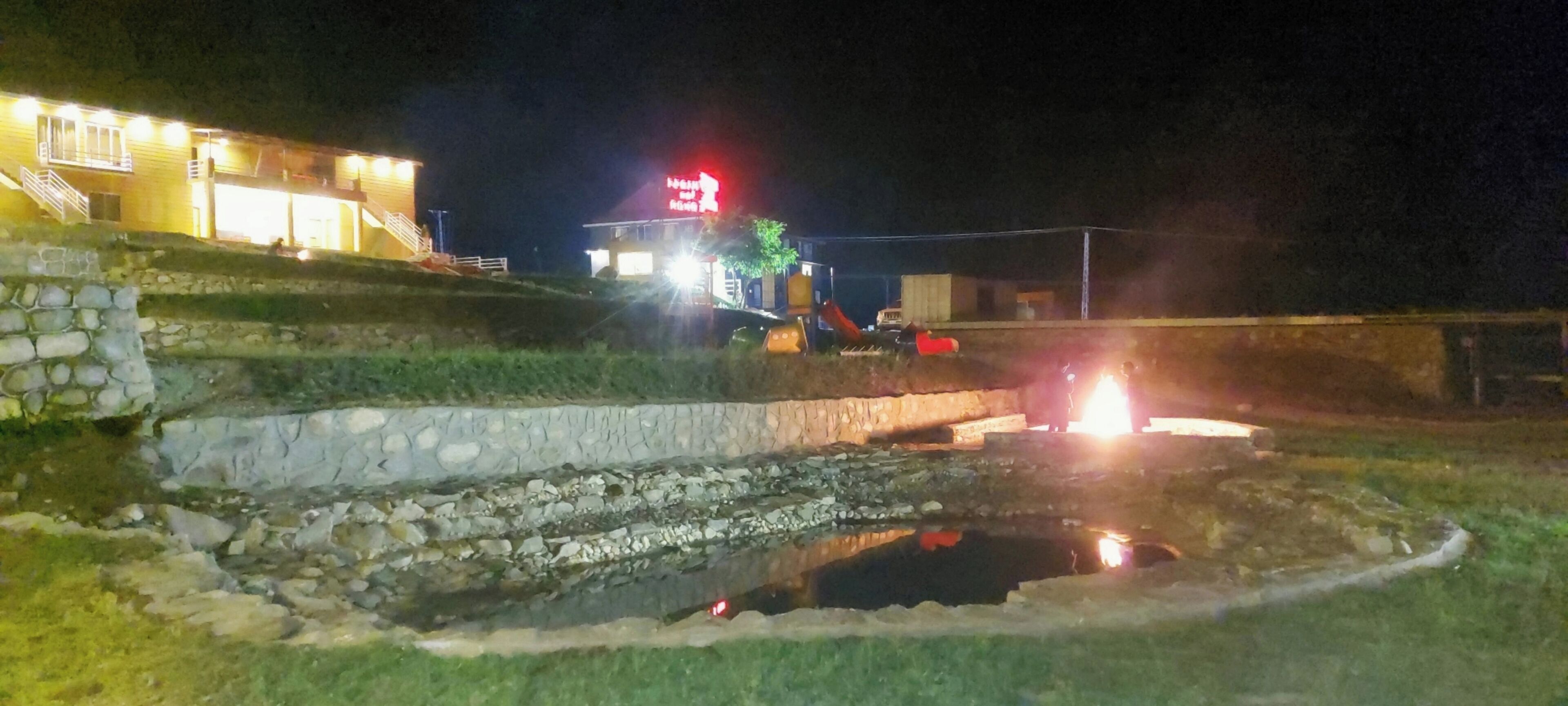 Escena nocturna con un edificio que tiene una escalera y un pequeño estanque.
