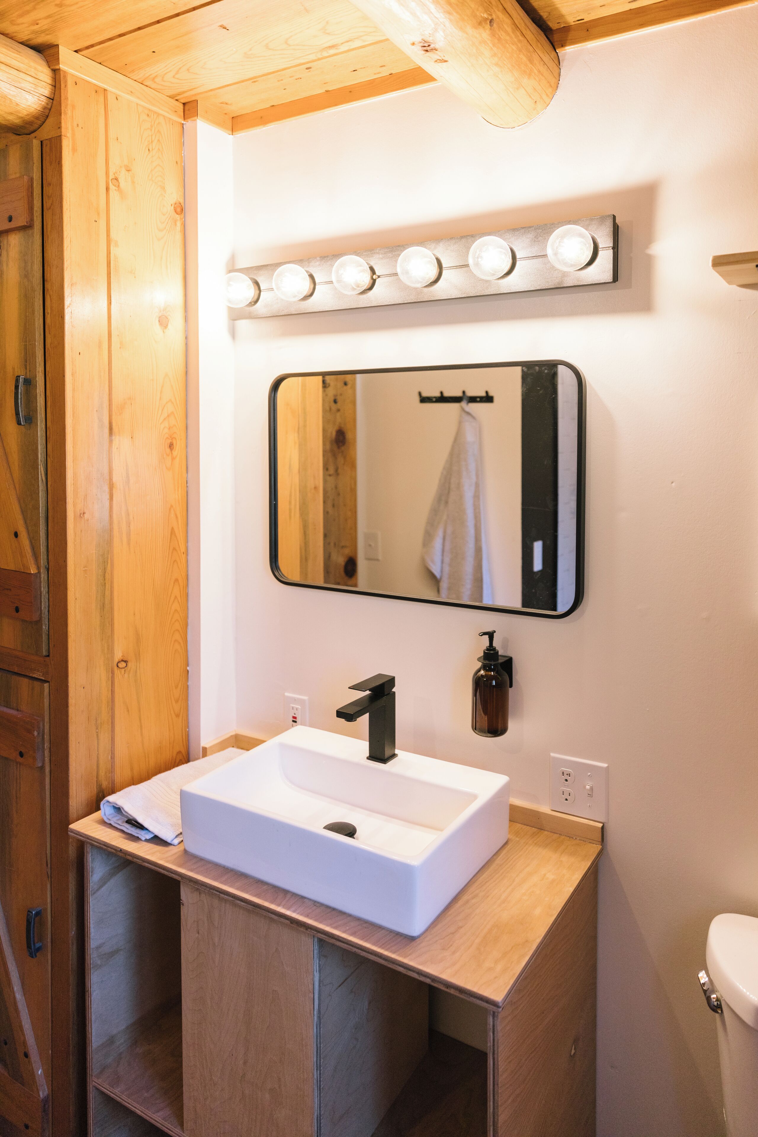 Ein Badezimmer mit einem Holzkosmetikschrank, einem weißen Waschbecken, einem Spiegel mit Beleuchtung darüber und einer Toilette.