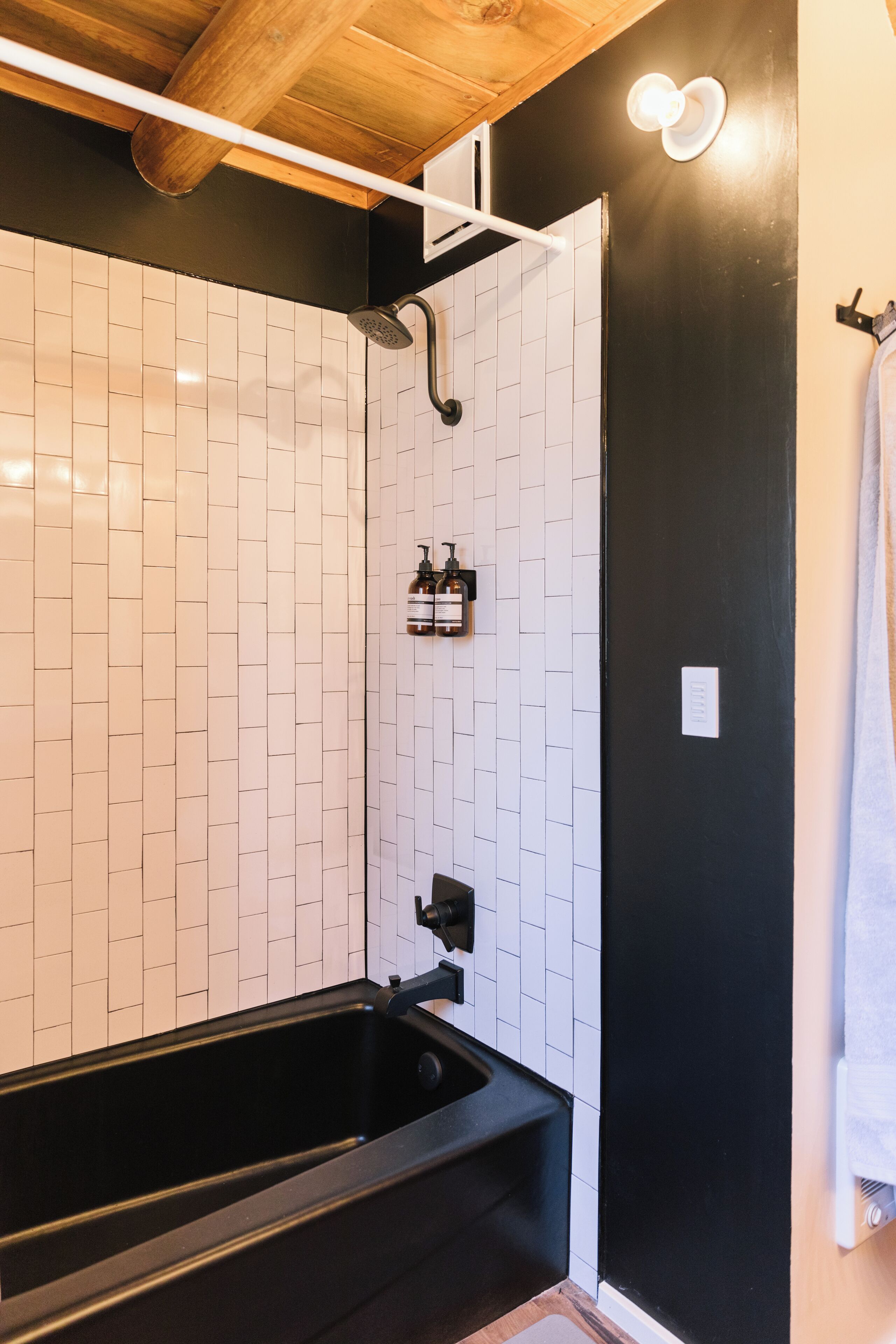 Une salle de bain moderne avec une baignoire noire, des murs recouverts de carreaux blancs et un plafond en bois.