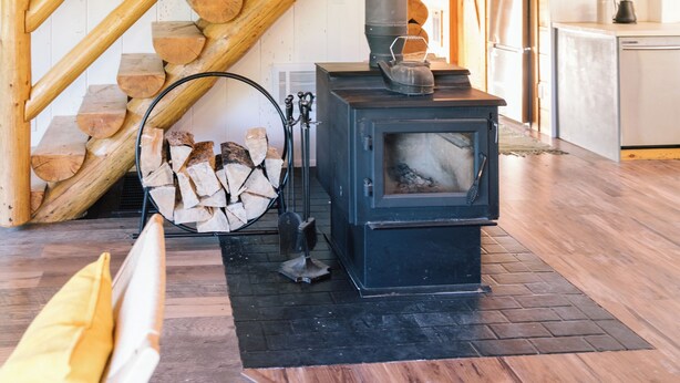 A wooden interior with a wood stove, a staircase, and a kitchen area.