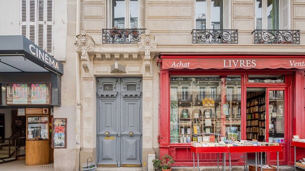 Une devanture de magasin avec un auvent rouge sur lequel on peut lire « ACHAT LIVRES » et un panneau indiquant qu’il s’agit d’un cinéma, placé au-dessus.