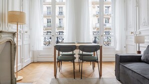 Une pièce dotée d’un plancher en bois, d’une table avec deux chaises, d’un canapé et offrant une vue sur des balcons à travers une série de portes blanches.