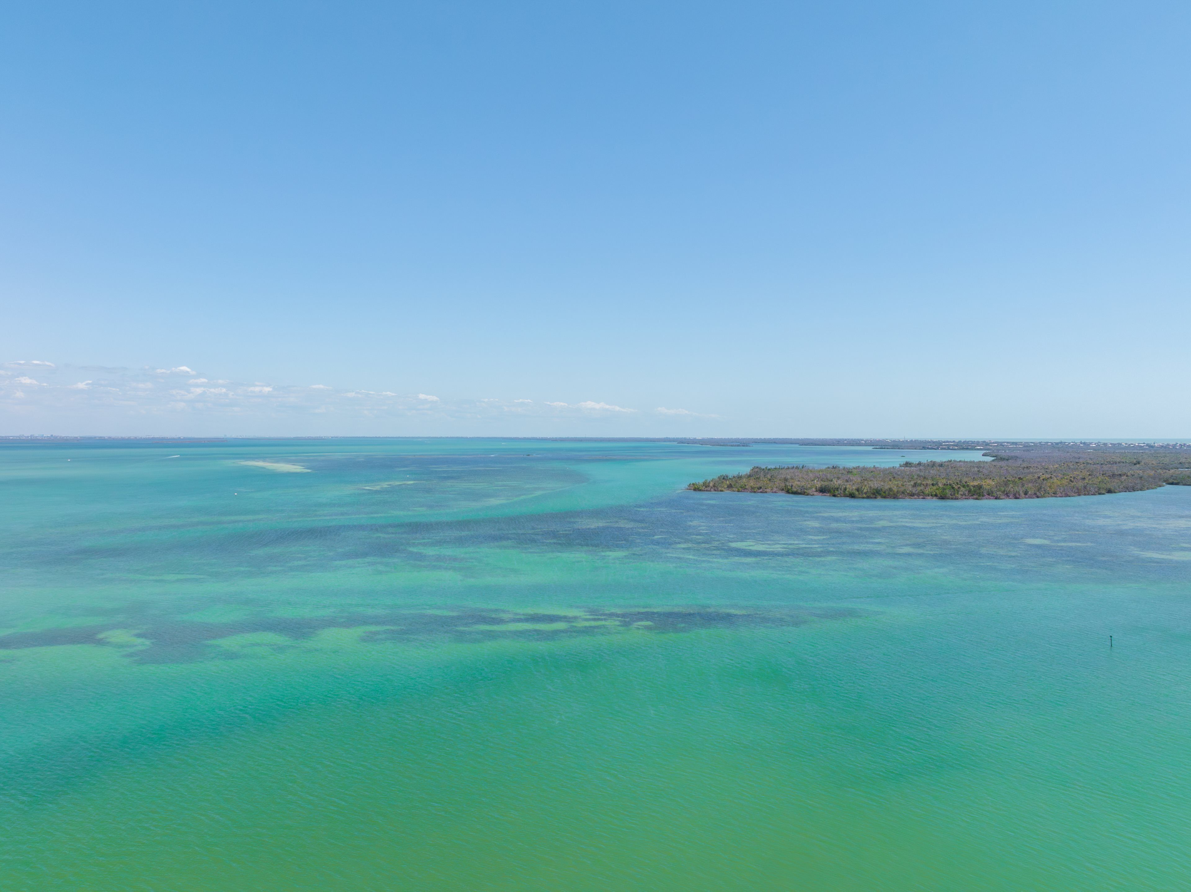 An aerial view of a coastal area with clear turquoise waters and a small island with dense vegetation.