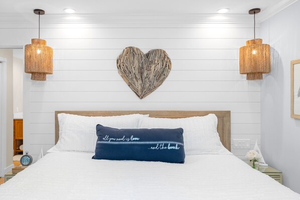 A neatly made bed with a decorative pillow, a heart-shaped wall art, and two hanging light fixtures. - Family Favorite | Sleeps 8, Heated Pool, Game Room, Steps to Captiva Fun (Captiva)