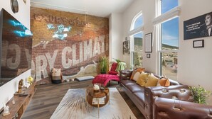 A spacious living room with a large brick wall mural, a leather sofa, and a wooden coffee table. - The Ghost Lounge (Victor)