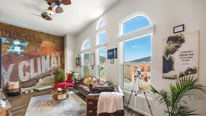 A modern living room with a brick wall mural, a leather sofa, a red couch, and a large window offering a view of the outdoors. - The Ghost Lounge (Victor)