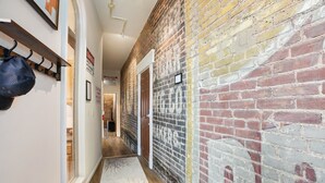 A hallway with a brick wall, a coat rack, and a door leading to another room. - The Ghost Lounge (Victor)