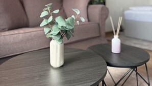 A living room with a sofa, two round tables, a small white vase with a plant, and a white diffuser with reed sticks.