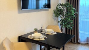 A dining area with a table set for two, a flat-screen TV mounted on the wall, and a potted plant.
