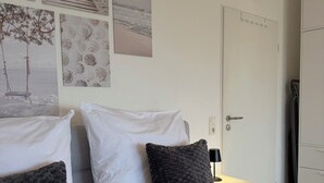 A bedroom with two beds, white bedding, a clock on the wall, and various framed pictures.