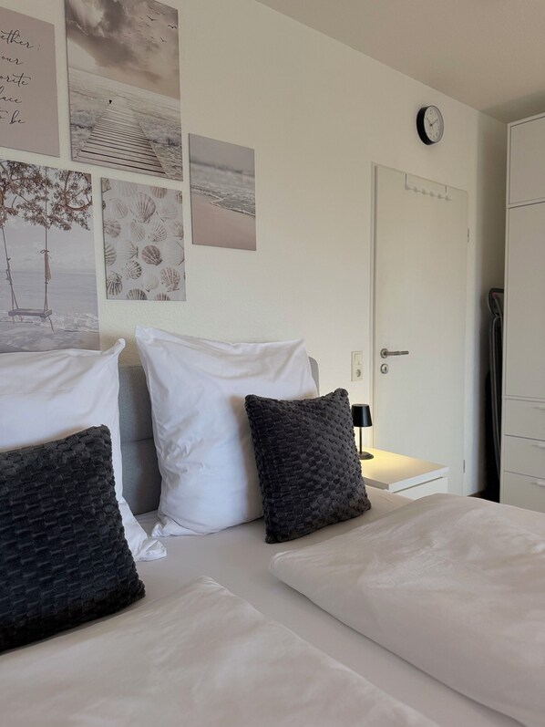 A bedroom with two beds, white bedding, a clock on the wall, and various framed pictures.