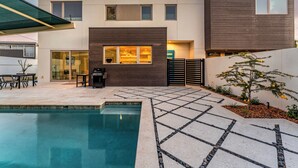 Ein modernes, zweistöckiges Haus mit Pool, Sitzgelegenheit im Freien und einem gepflegten Garten.