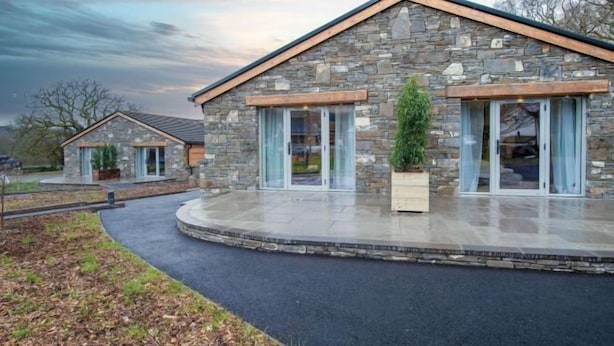 A modern stone house with a curved driveway and a small garden.