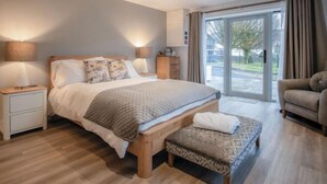A modern bedroom with a large bed, bedside lamps, a bench, and a view of the outdoors through a glass door.