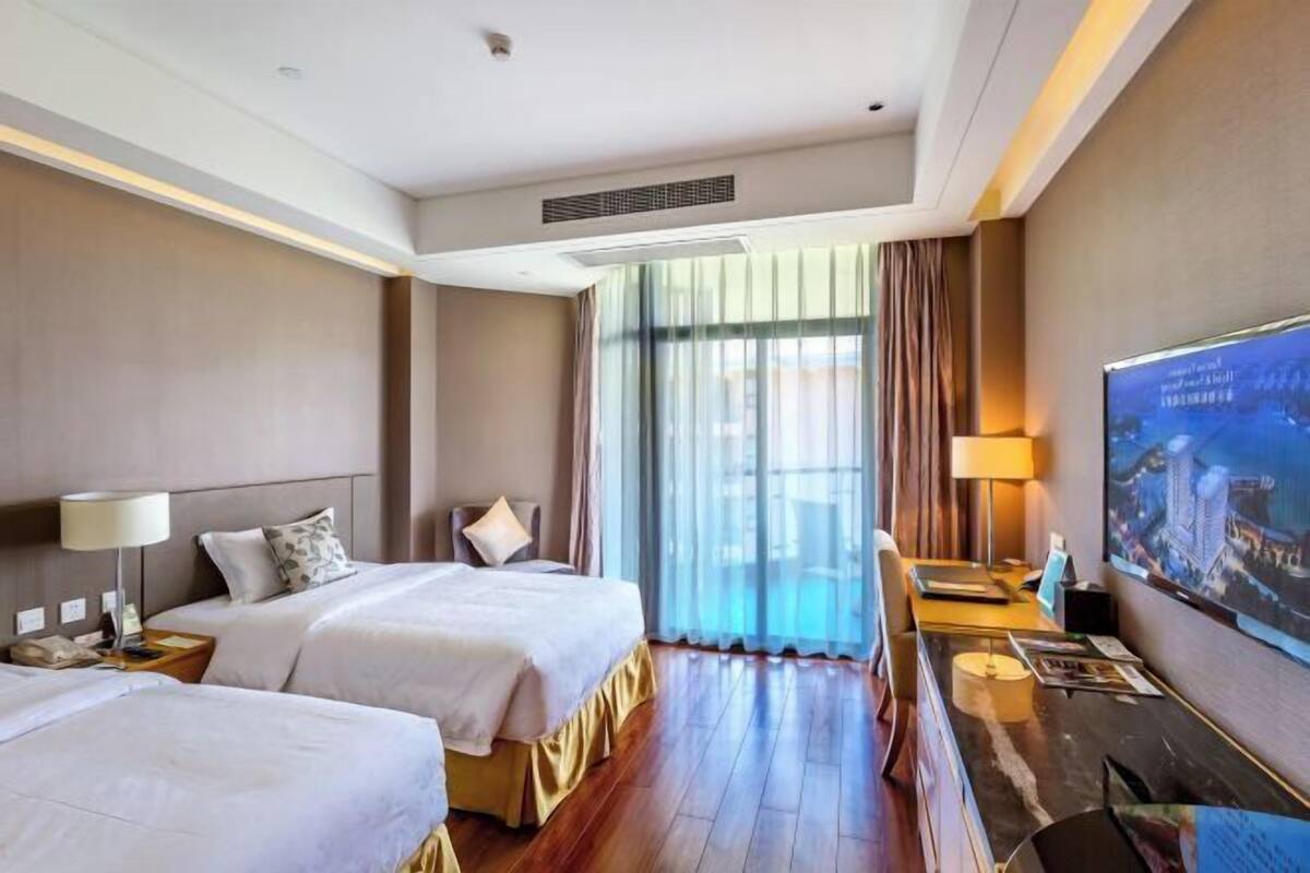 Habitación de hotel con dos camas, un escritorio, un televisor y un ventanal con cortinas.
