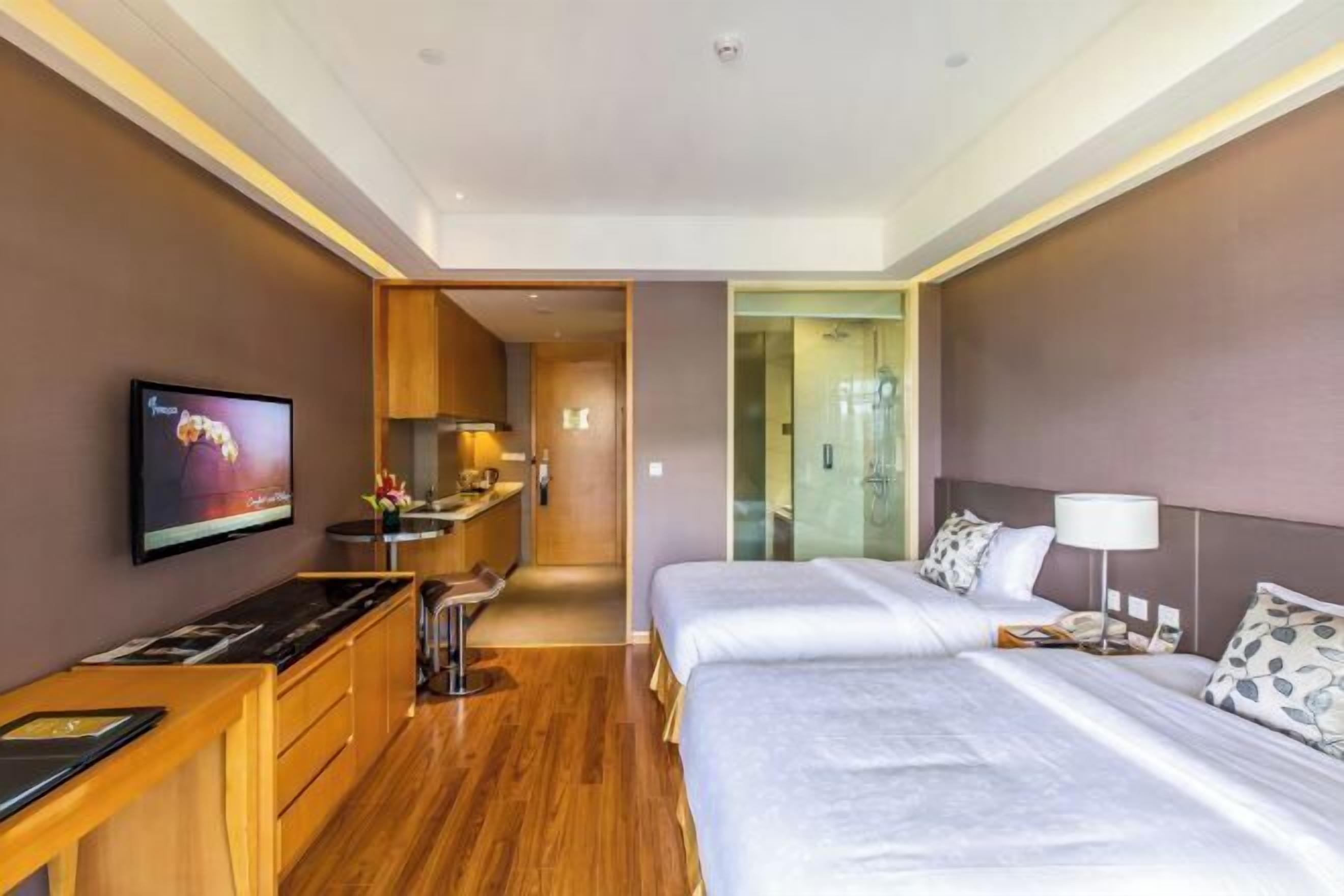 A hotel room with two beds, a desk, a TV, and a bathroom visible through a glass door.