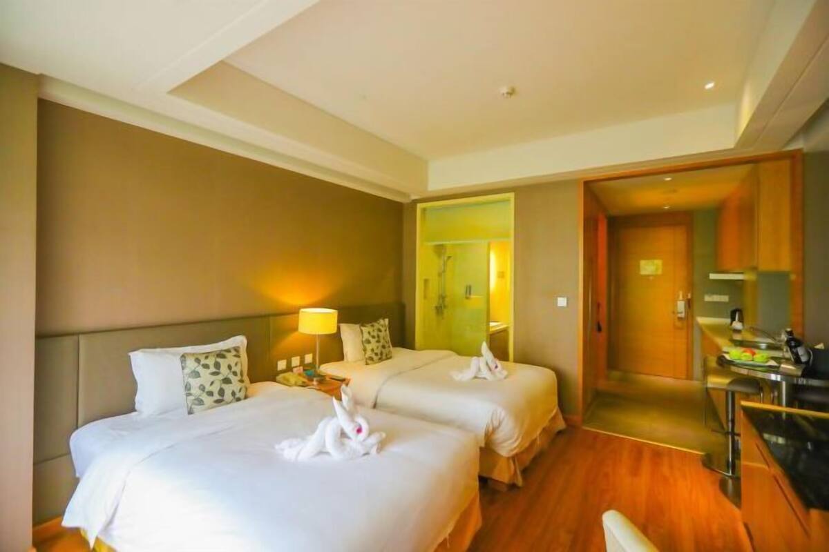 Habitación de hotel con dos camas, un escritorio y un baño visible a través de una puerta abierta.