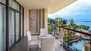 A balcony with white wicker chairs, a glass door, and a view of a pool and landscape.