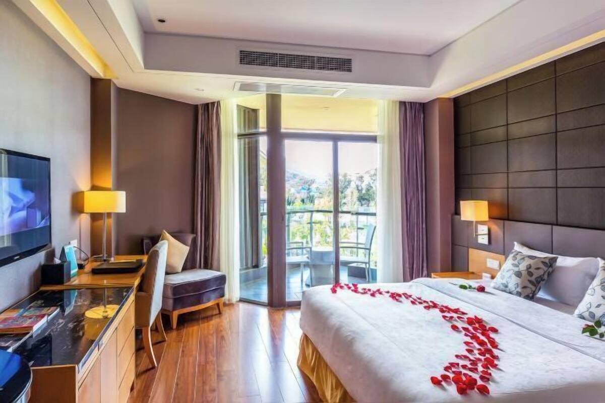 Habitación de hotel con una cama grande, un escritorio con silla, televisión y balcón con vistas.