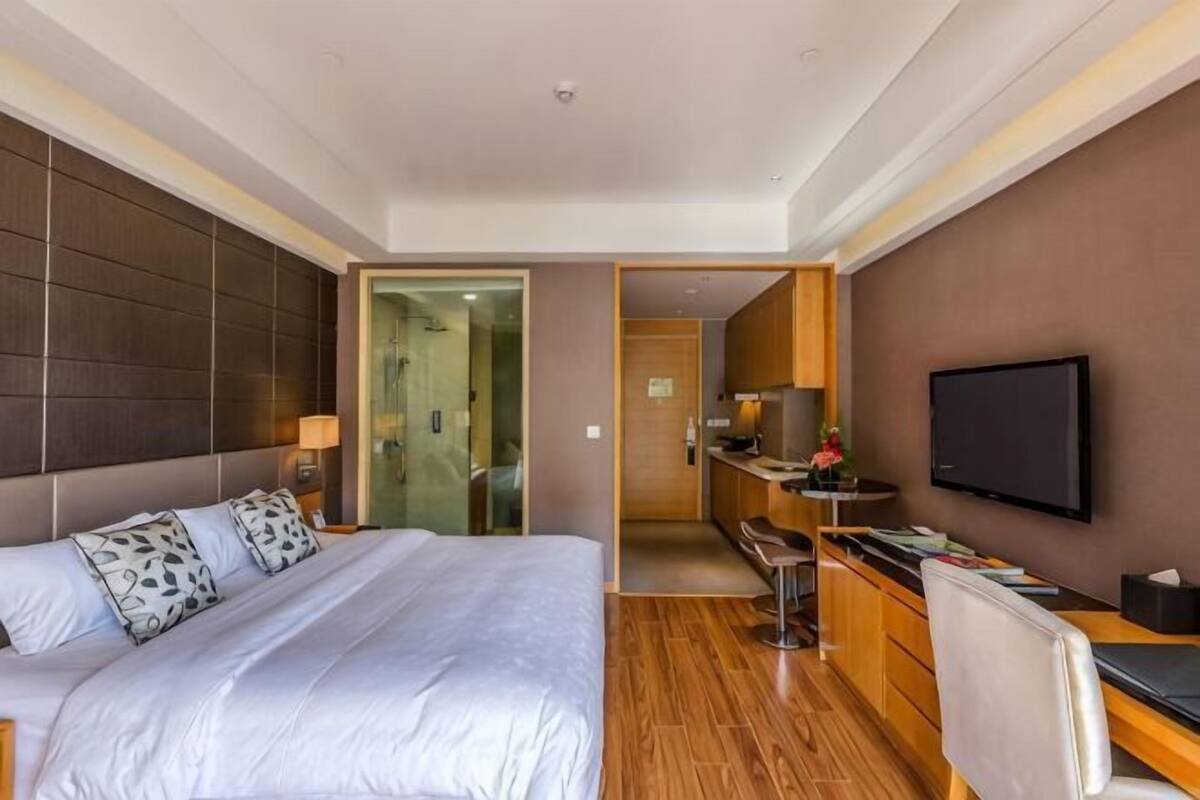 Habitación de hotel con una cama grande, un escritorio, un televisor y un baño visible a través de una puerta abierta.